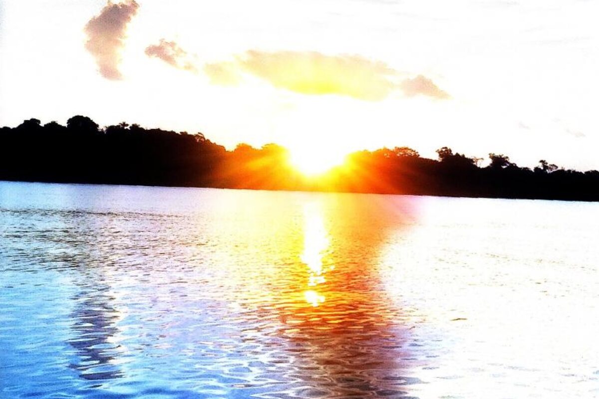 Sol nascendo sobre o rio, com a silhueta da floresta amazônica ao fundo